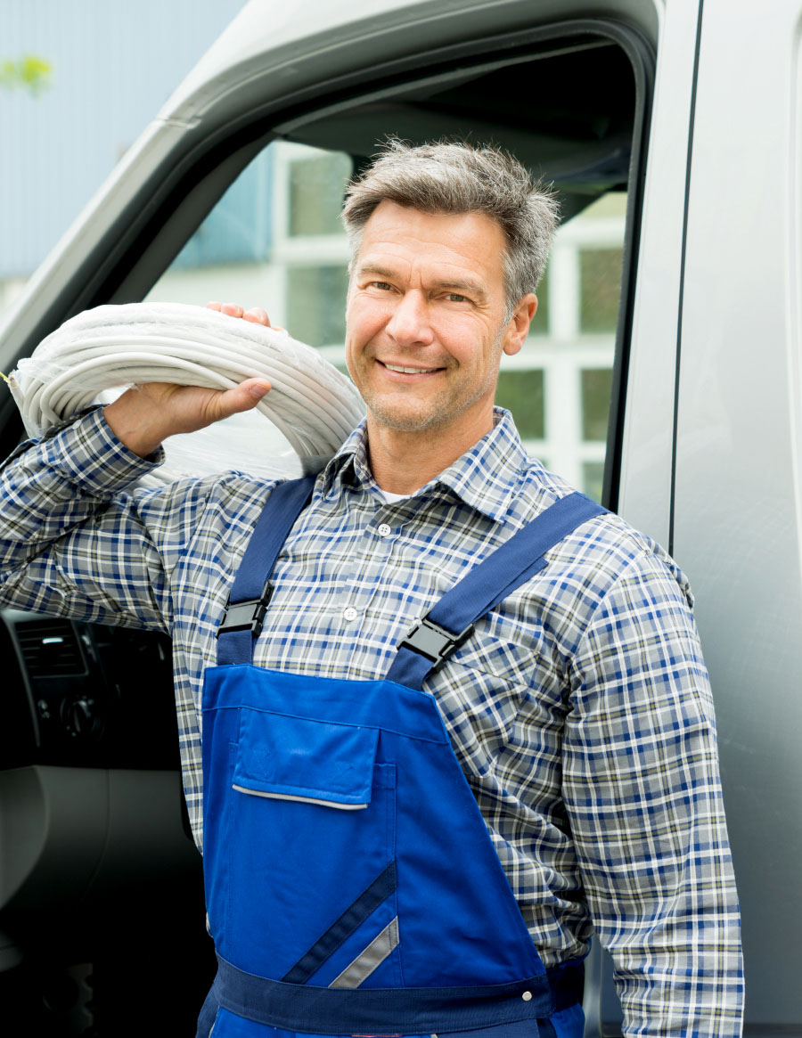 Worker in blue overalls carrying a coil of white cable on his shoulder by a van