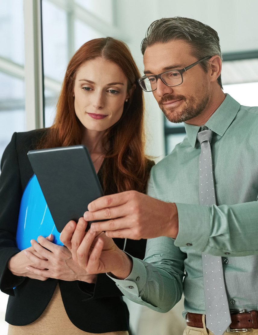 Man in a shirt and tie showing a tablet screen to a woman in a blazer