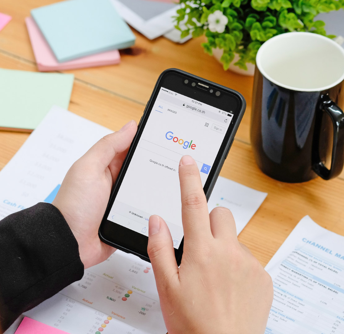 Hands using a phone on the Google search page above printed reports on a desk