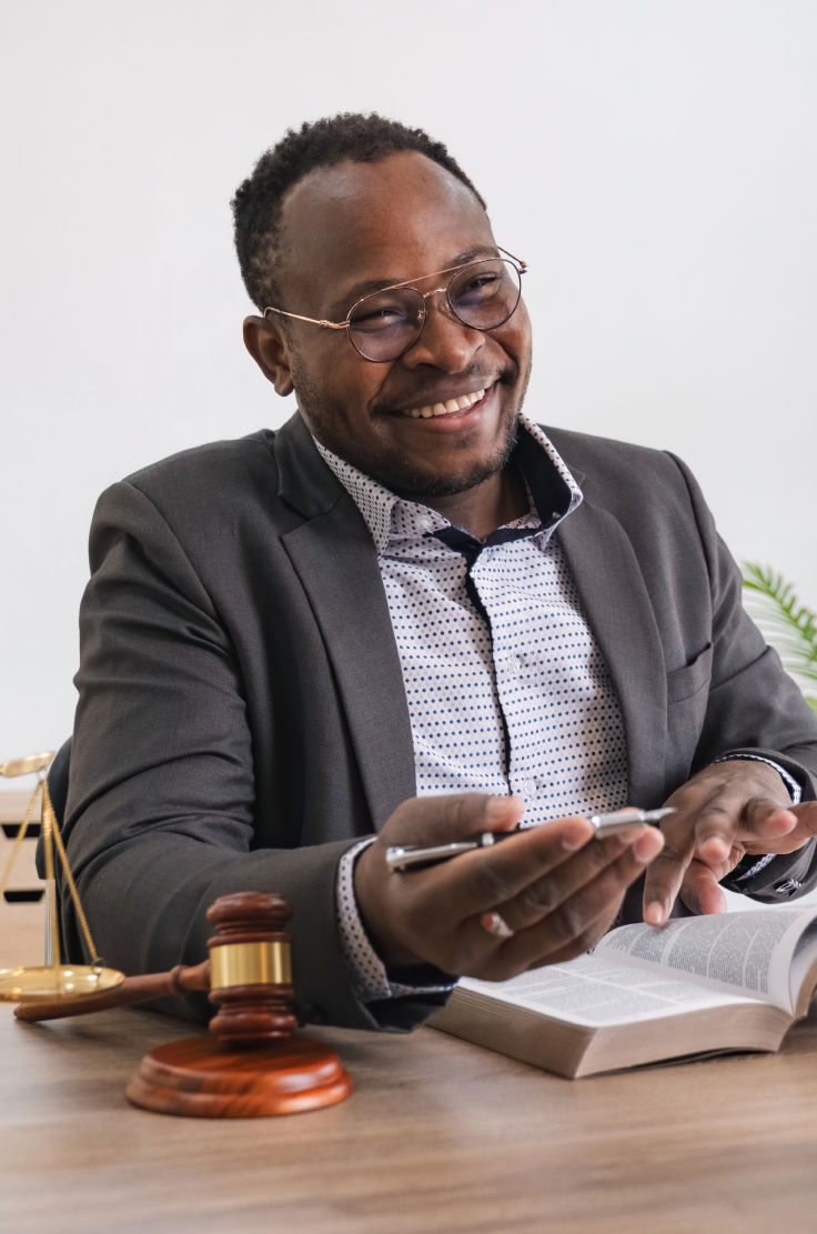 Smiling man in a suit at a desk with a gavel, scales of justice and an open law book
