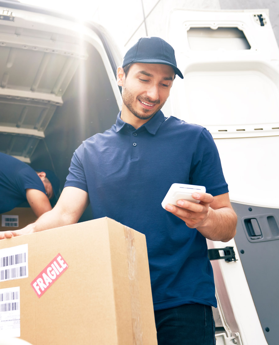 Delivery worker holding a cardboard box labelled Fragile while checking a handheld scanner at an open van